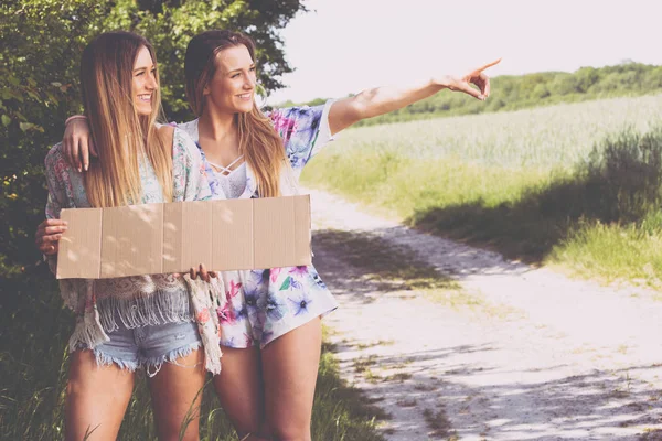 Дві дівчини друзі чекають з паперовою тарілкою, щоб автостоп — стокове фото
