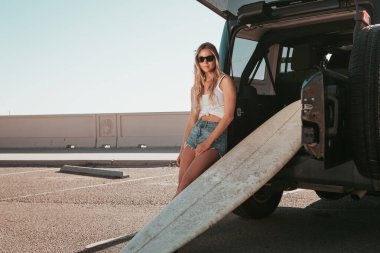 Sörf tahtasıyla arabada oturan sörfçü kız. California yaşam tarzı