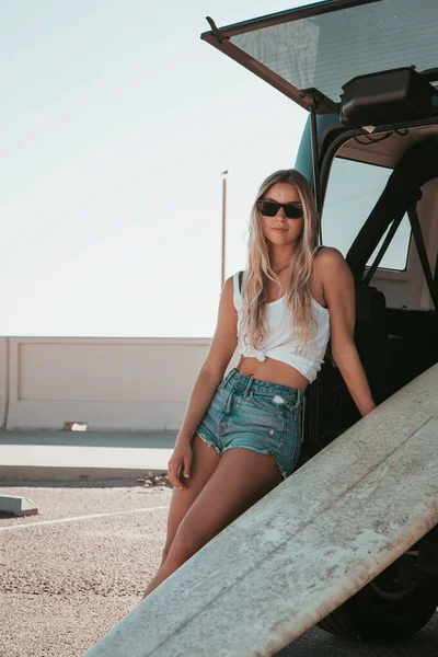 Surfermädchen sitzt an einem Auto mit Surfbrett. kalifornischer Lebensstil — Stockfoto