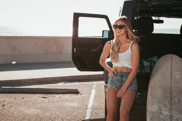 Surfer meisje zit aan een auto met surfplank. california levensstijl — Stockfoto