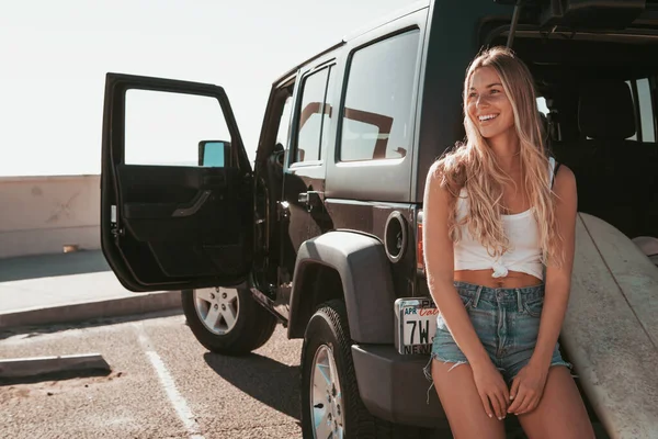 Surfista chica sentada en un coche con tabla de surf. estilo de vida california —  Fotos de Stock