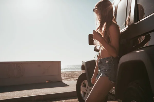 Surfer meisje staat bij een auto op het strand. california levensstijl — Stockfoto