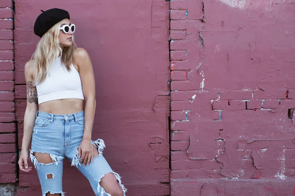 Jonge vrouw staan door een muur met zonnebril en zwarte hoed — Stockfoto