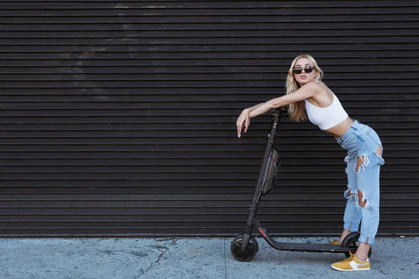 Eine junge Frau steht mit ihrem E-Roller an einer Mauer. umweltfreundlich — Stockfoto