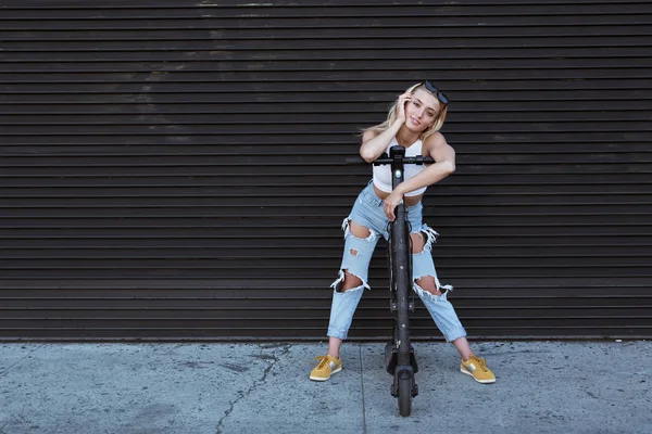 Mujer joven de pie junto a una pared con un e-scooter. respetuoso del medio ambiente —  Fotos de Stock