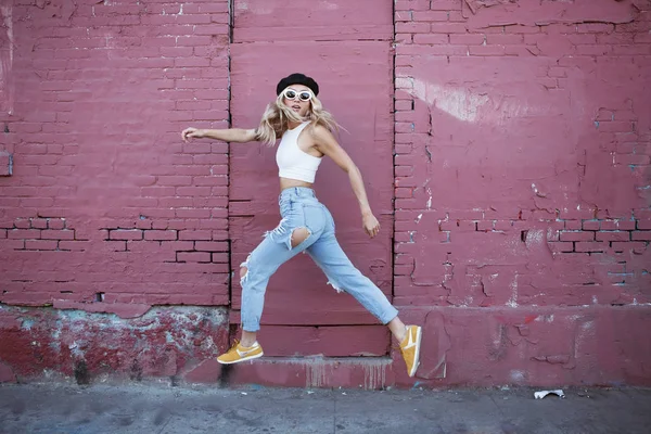 Mujer joven saltando por una pared con gafas de sol y sombrero negro —  Fotos de Stock