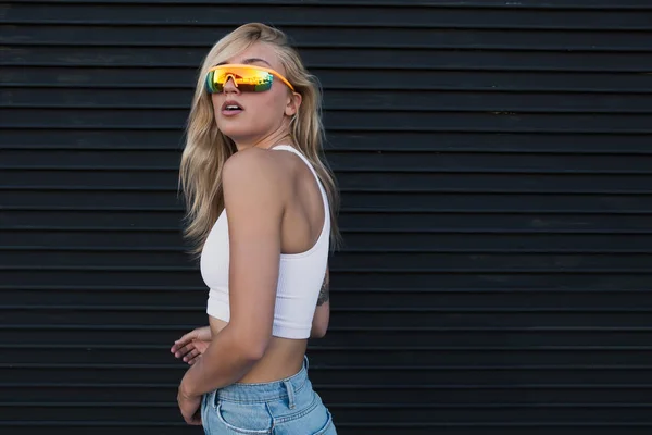 Jonge vrouw staan door een zwarte muur met zonnebril — Stockfoto