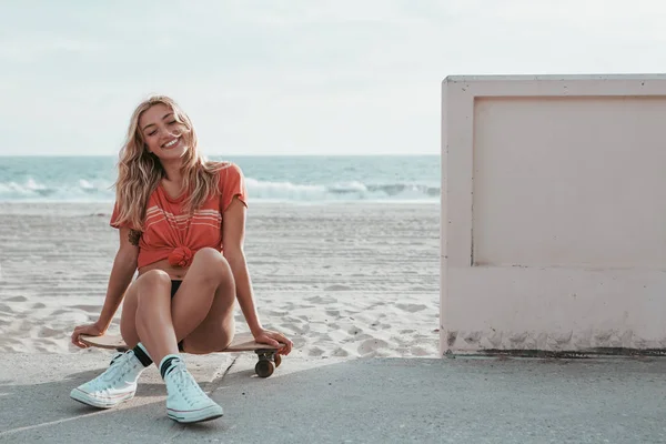 Skater menina sentado em um skate na praia malibu — Fotografia de Stock