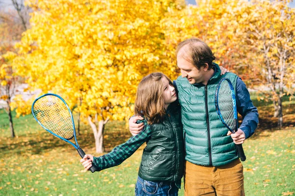 Father and son in the autumn park with tennis rackets