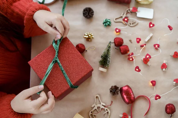Egy piros pulóveres gyerek kinyitja a piros ajándékdobozt. — Stock Fotó