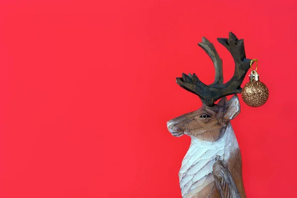 Reno de madera de Navidad divertido con pequeña bola festiva sobre un fondo rojo — Foto de Stock