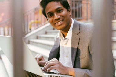 Genç ve yakışıklı Hintli adam merdivenlerde oturuyor.