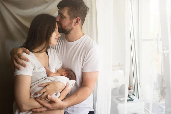 Baba ve anne ve yeni doğmuş bir çocuk pencerenin önünde duruyor.