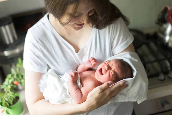 Una madre con un neonato tra le braccia lo sta allattando in cucina — Foto Stock