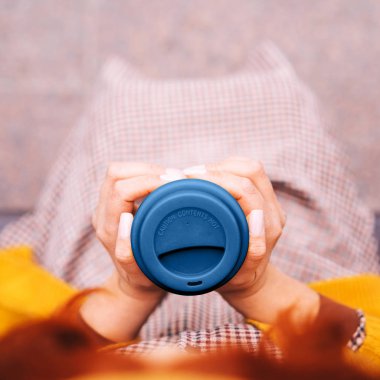 Kızıl saçlı bir kadın bir bankta oturuyor ve elinde bambu kabıyla