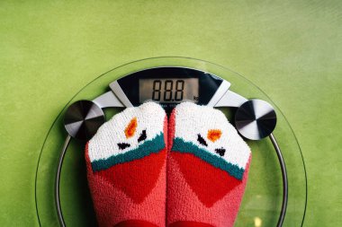 Girl standing on the scales in Christmas fun red green socks with snowman clipart