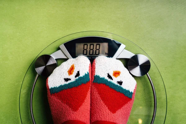 Girl standing on the scales in Christmas fun red green socks with snowman — Stock Photo, Image