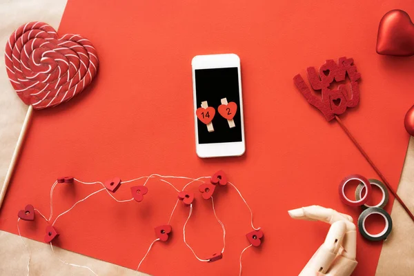Szív alakú nagy piros-fehér csíkos cukor nyalóka, fa kéz, telefon — Stock Fotó