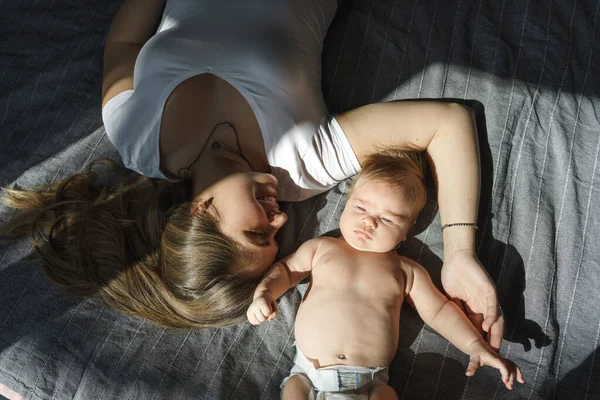 Madre con su hijo recién nacido yacía en la cama bajo los rayos del sol —  Fotos de Stock