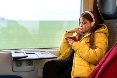 Kafasında kulaklıkla banliyö treninde oturan genç bir kız.