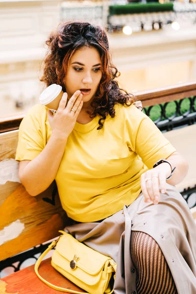 Beautiful cheerful curly woman in a bright yellow sweater with a handbag