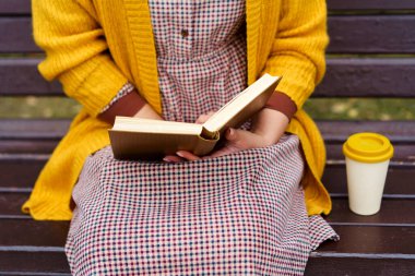 Bir kadın parkta bankta oturuyor ve elinde bir kitap tutuyor.