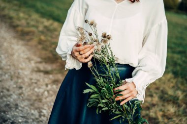 Genç bir kadın tarlada elinde yumuşacık bir sonbahar karahindiba dalını tutuyor.