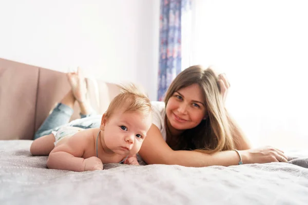 Madre con su hijo recién nacido yacía en la cama bajo los rayos del sol —  Fotos de Stock