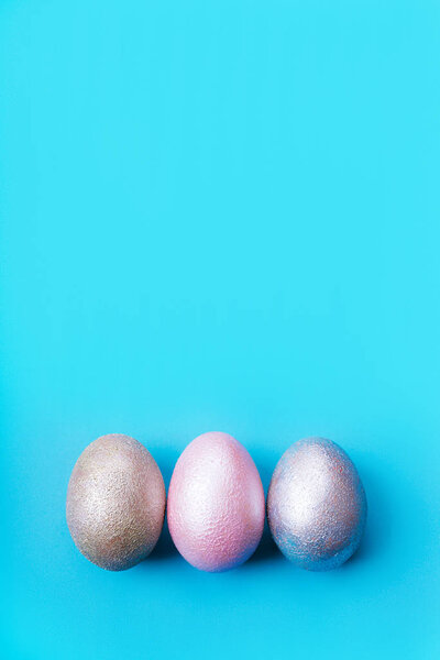 Three colored chicken eggs of pink, silver, golden on blue color background 