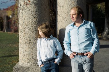  Father and son standing on a sunny summer day in the shade under a column