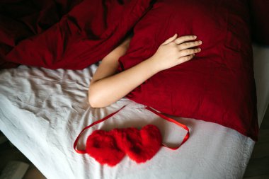 Female hand lying on a red pillow covered with a blanket.