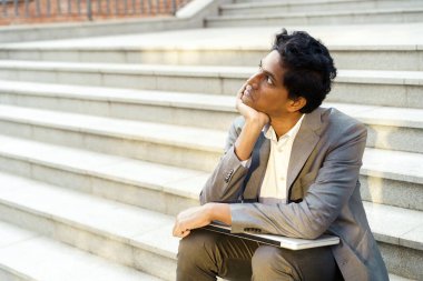 Genç ve yakışıklı Hintli bir adam dizüstü bilgisayarıyla oturuyor, gülümsüyor ve yazıyor.