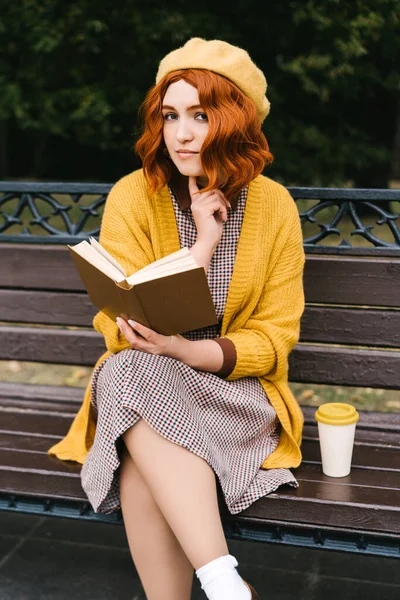 Ένα όμορφο κορίτσι με σγουρό χτένισμα κάθεται σε ένα παγκάκι και διαβάζει — Φωτογραφία Αρχείου