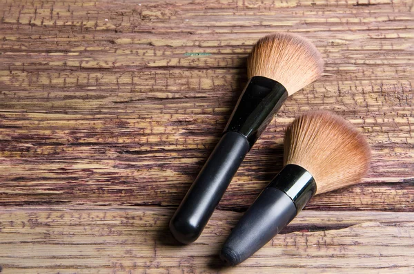 Escovas para maquiagem espalhadas caoticamente sobre fundo de madeira — Fotografia de Stock