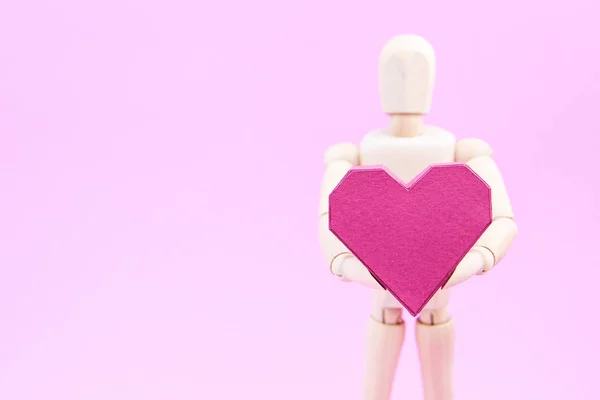 Maniquí de madera que sostiene la caja de papel en forma de corazón rojo sobre fondo rosa — Foto de Stock