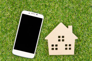 Ahşap ev oyuncak ve Smartphone ile kopya yere yeşil çimenlerin üzerinde 