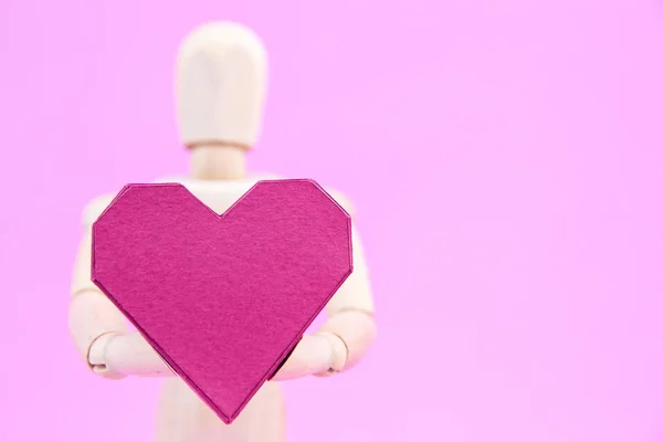 Maniquí de madera que sostiene la caja de papel en forma de corazón rojo sobre fondo rosa — Foto de Stock