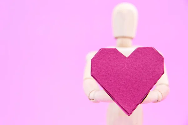 Maniquí de madera que sostiene la caja de papel en forma de corazón rojo sobre fondo rosa — Foto de Stock