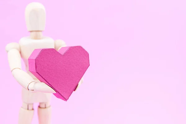 Maniquí de madera que sostiene la caja de papel en forma de corazón rojo sobre fondo rosa — Foto de Stock