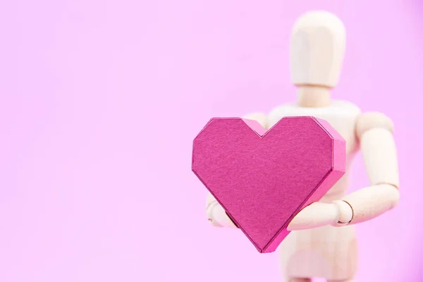 Maniquí de madera que sostiene la caja de papel en forma de corazón rojo sobre fondo rosa — Foto de Stock