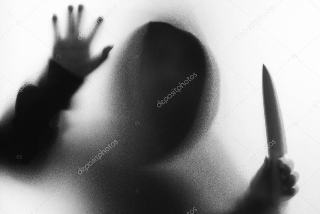 Shadow blur of horror man in jacket with hood knife in his hand.