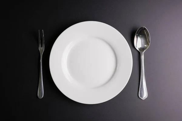 Plato blanco, cuchara y tenedor aislados sobre fondo negro con poli — Foto de Stock