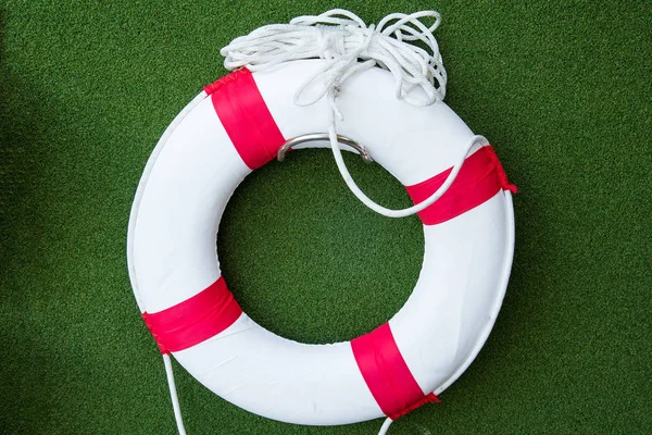 Boya salvavidas roja blanca con cuerda en pared de césped artificial verde . —  Fotos de Stock