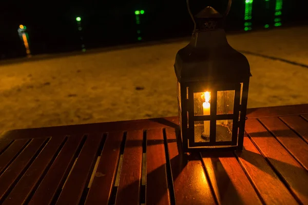 A candle lamp on a table by the sea at night.