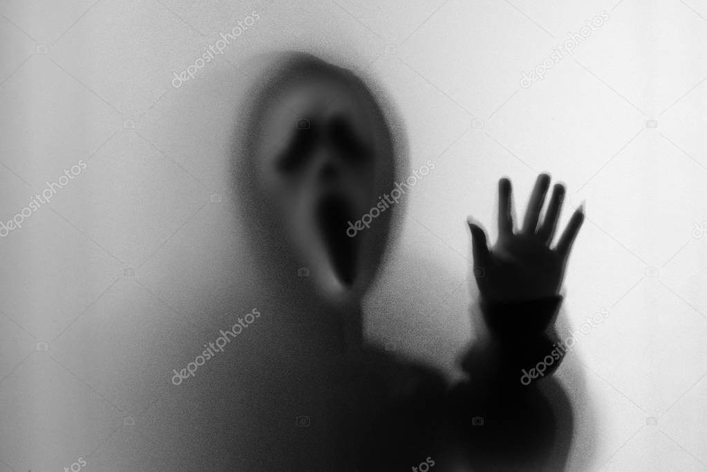 Shadow blur of horror man in screaming mask and hand touches the