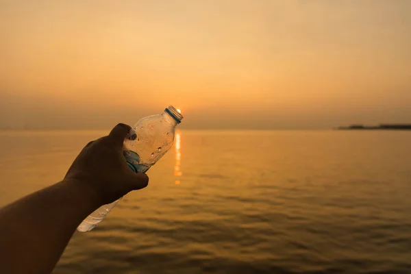 Мужчина держит бутылку питьевой воды в золотой час заката — стоковое фото