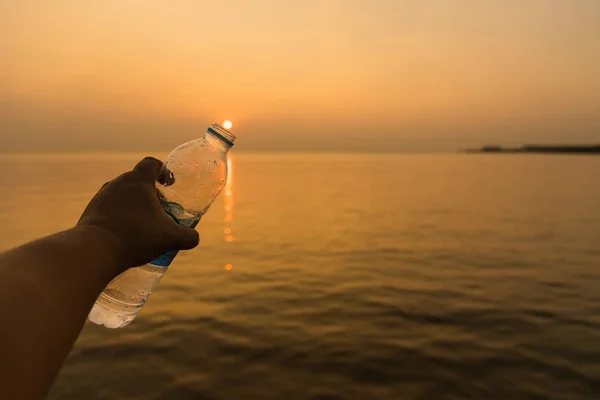 La mano del hombre sosteniendo la botella de agua potable en la hora dorada puesta del sol bac —  Fotos de Stock