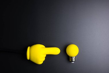 Siyah arka plan üzerinde gösteren bir ampul ve sarı plastik el 