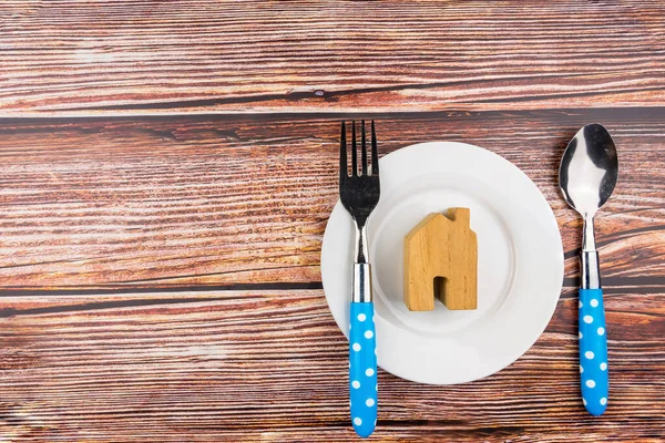 Casa in legno in piatto bianco e forchetta, cucchiaio sul tavolo in legno indietro — Foto Stock