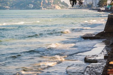 Dalgalı yeşil deniz. Siyah kaya ve kahverengi kum.
